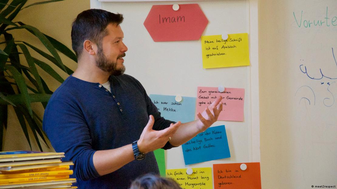 Imam Ender Cetin gesticulates against a colourful background in a classroom setting