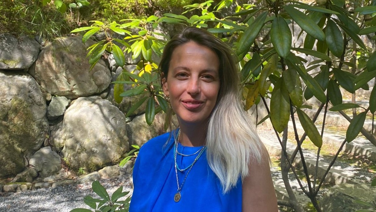 Portrait of a woman in blue against a leafy background and a stone wall