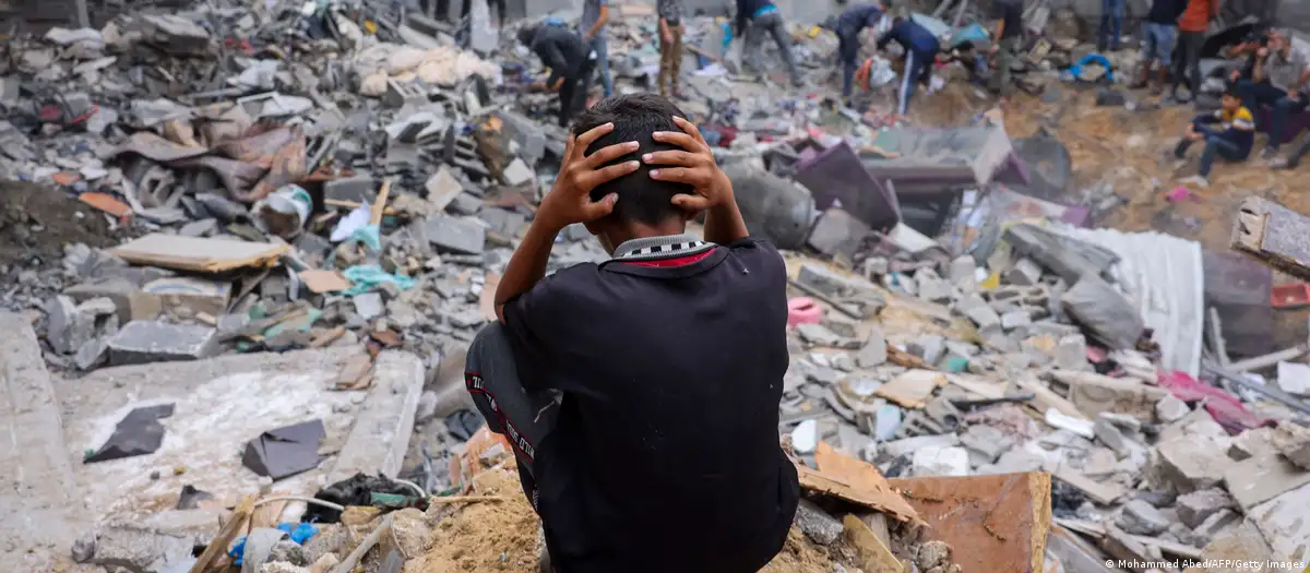 A child sits with his head in his hands as people salvage belongings from the rubble of a damaged building following strikes on Rafah, Gaza Strip, 12 November 2023