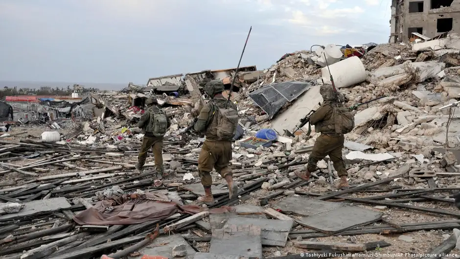 مساحات واسعة من المباني في قطاع غزة لحقه الدمار في حرب إسرائيل على حماس في القطاع. Three Israeli soldiers, armed and in fatigues, walk through rubble in the Gaza Strip 