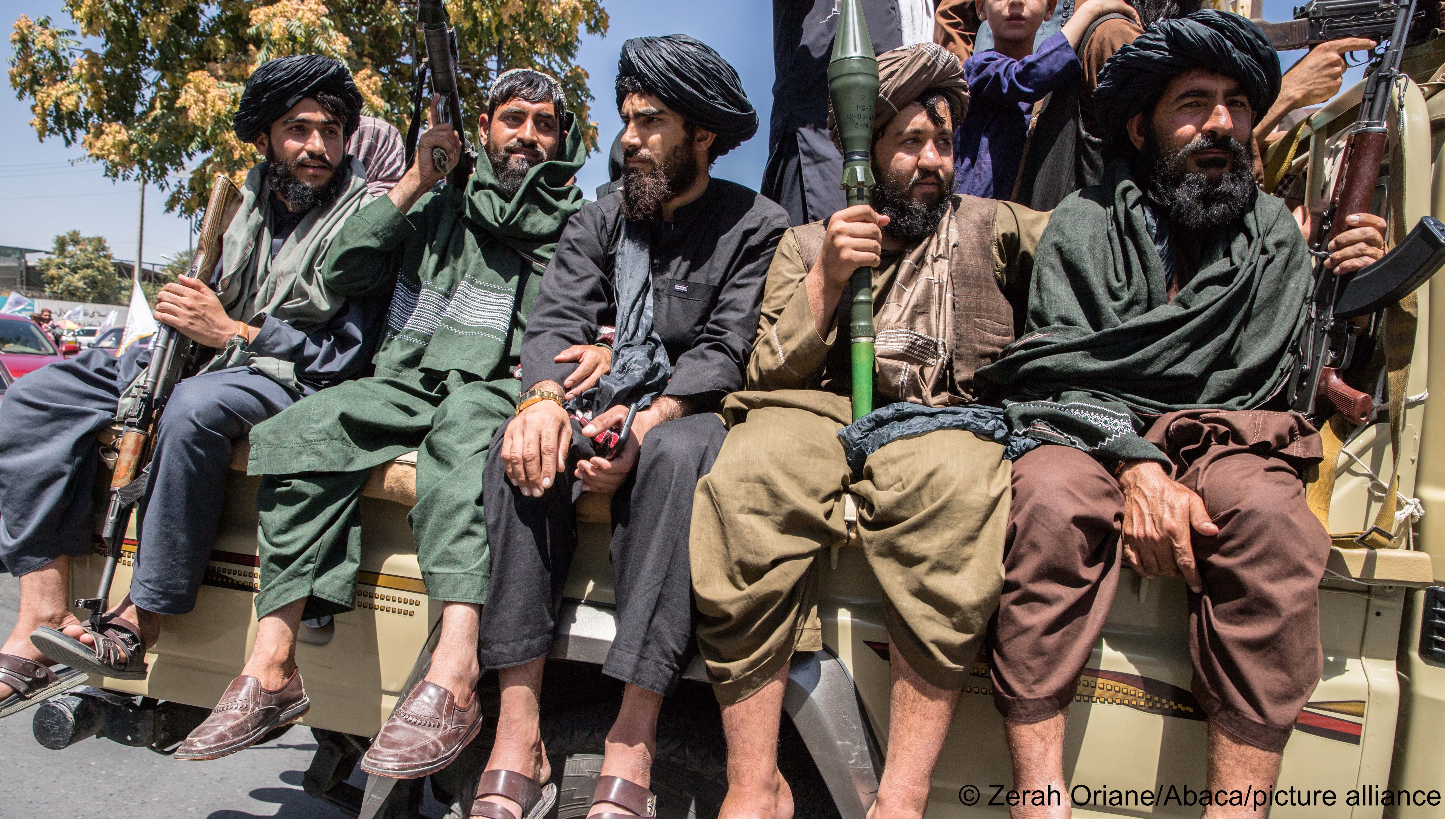 Men bearing arms sit on the back of a truck. Taliban and Taliban supporters gathered in front of the American embassy in Kabul on 15 August 2023 to celebrate the second anniversary of their takeover of the country