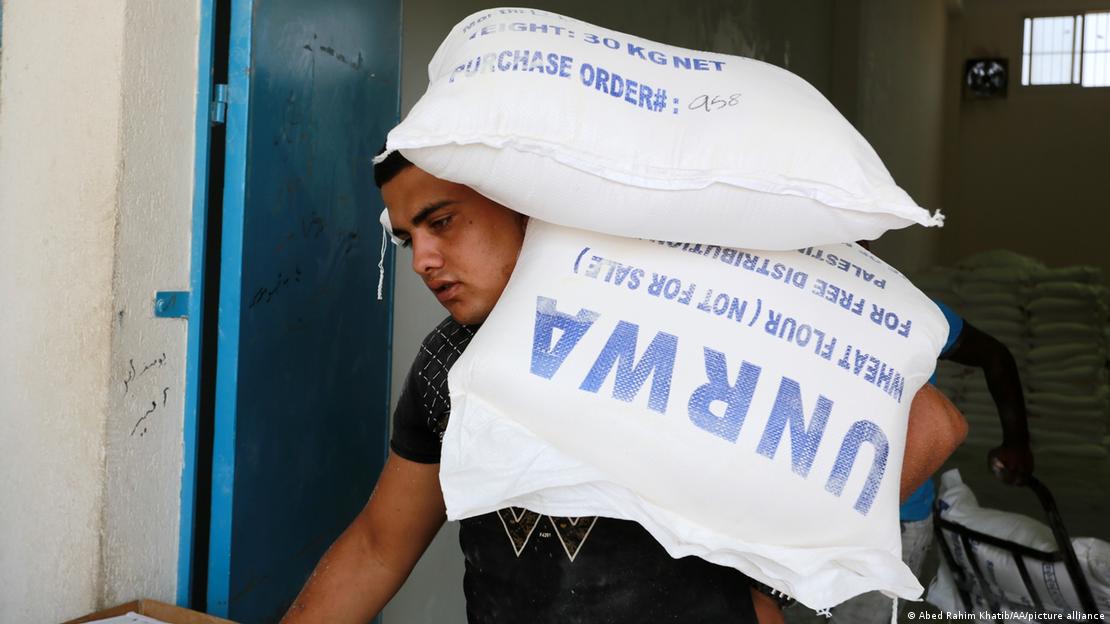 A man carries two UNRWA sacks of wheat flower on his shoulder as he walks through a blue door