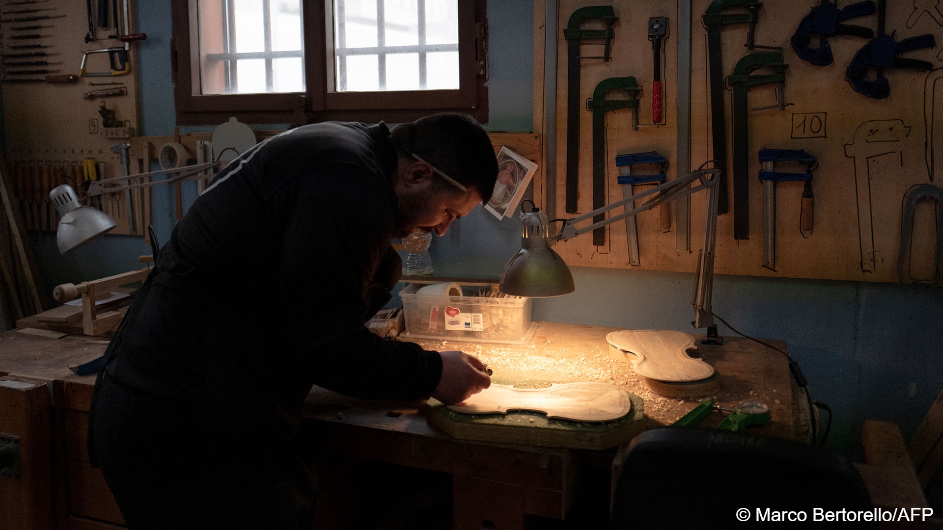 An inmate works on a piece of wood salvaged from a migrant boat to make a violin 