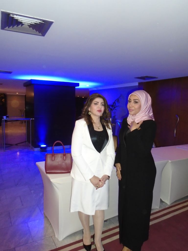 Nibras Al Mamory (left) and a woman in a pale pink headscarf stand at a table