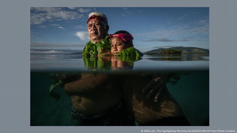 A man and a boy stand side by side in water, their torsos visible under the waterline