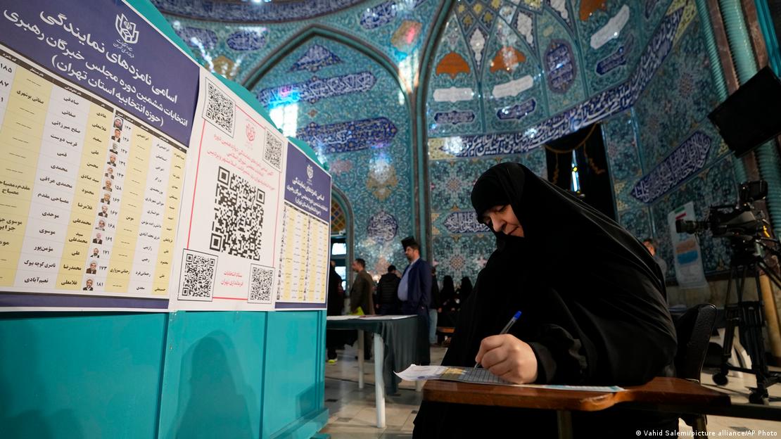 A woman holds a pen in her hand as she looks at a ballot paper at a polling station in Iran