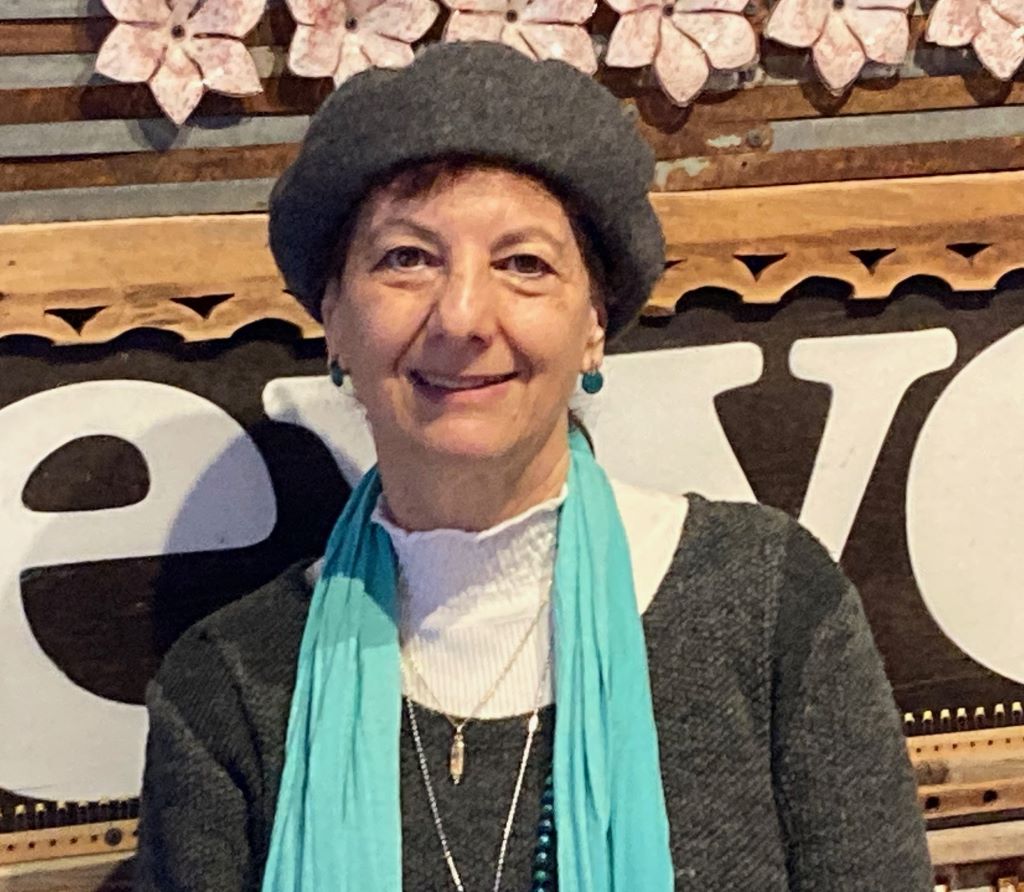 Headshot of a smiling woman (Peta Jones Pellach) wearing a grey beret and a turquoise scarf