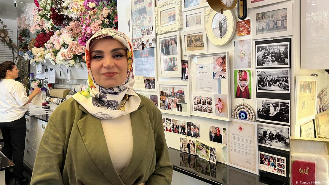 A woman stands in her shop in front of pictures and awards, smiling into the camera