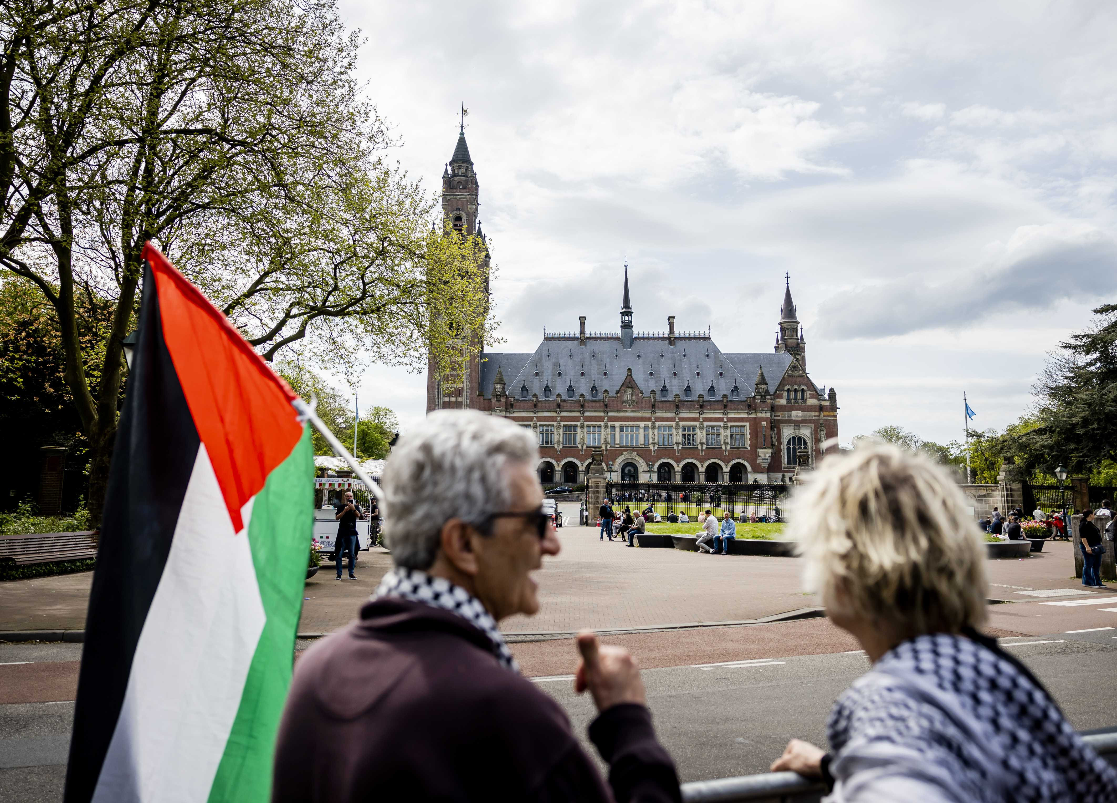 A man with a Palestinian flag and a woman stand in front of the International Court of Justice in The Hague