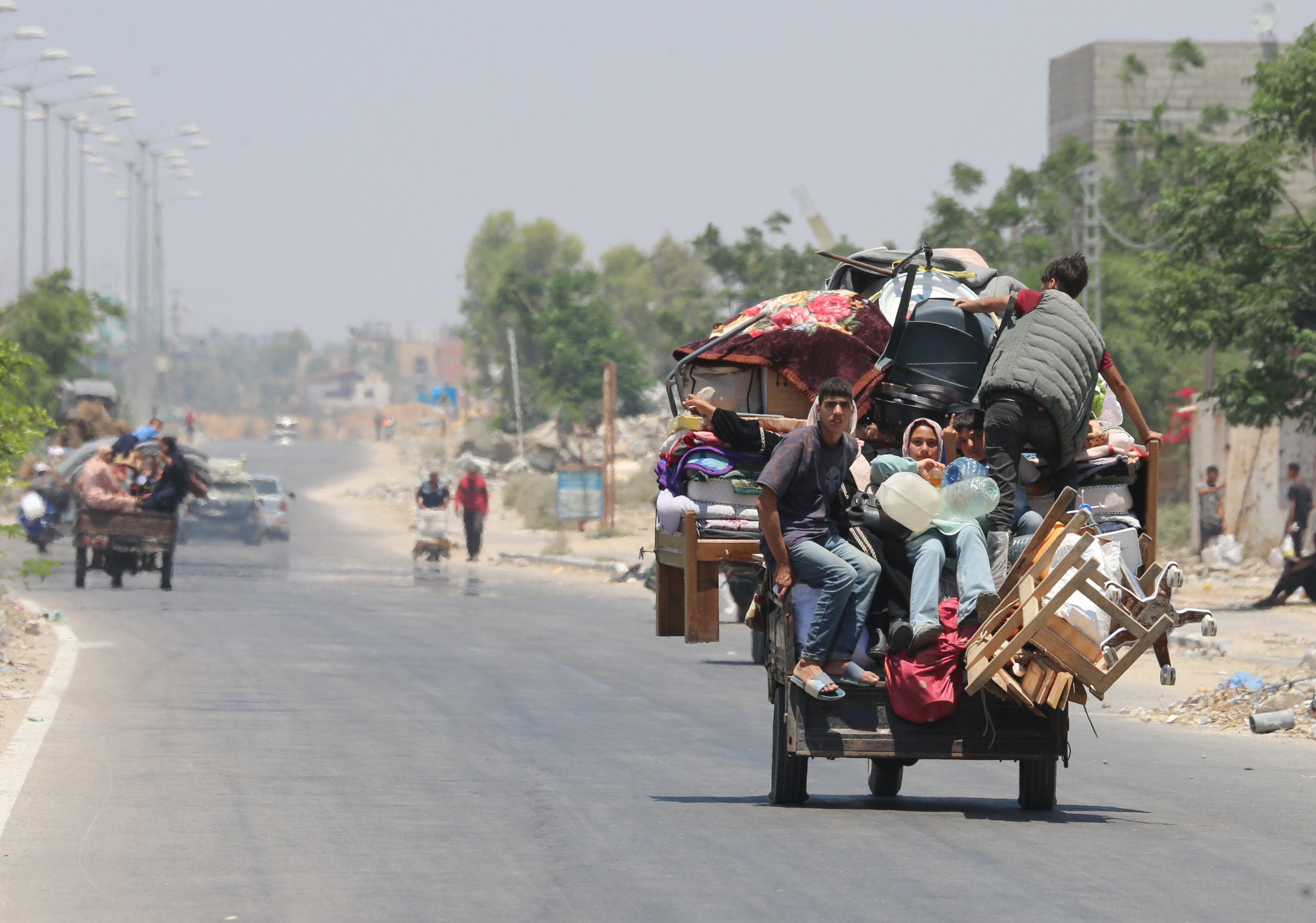 Junge Menschen in Gaza sitzen auf einem mit Möbeln und anderen Habseligkeit bepacktem Karren und verlassen die zerstörte Stadt