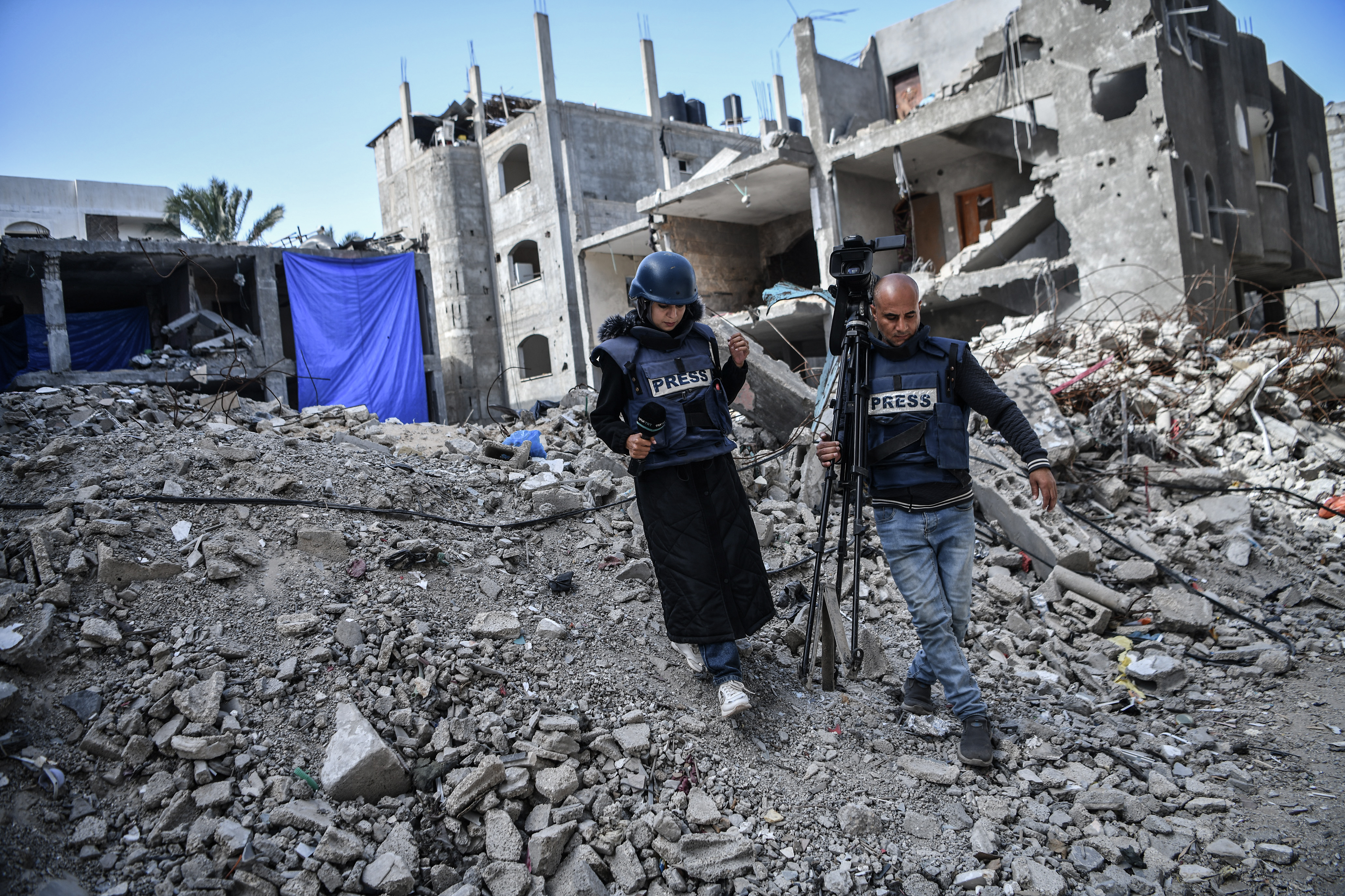 Blick auf zerstörte Häuser im Gazastreifen. Im Vordergrund laufen eine Journalistin und ein Kameramann.