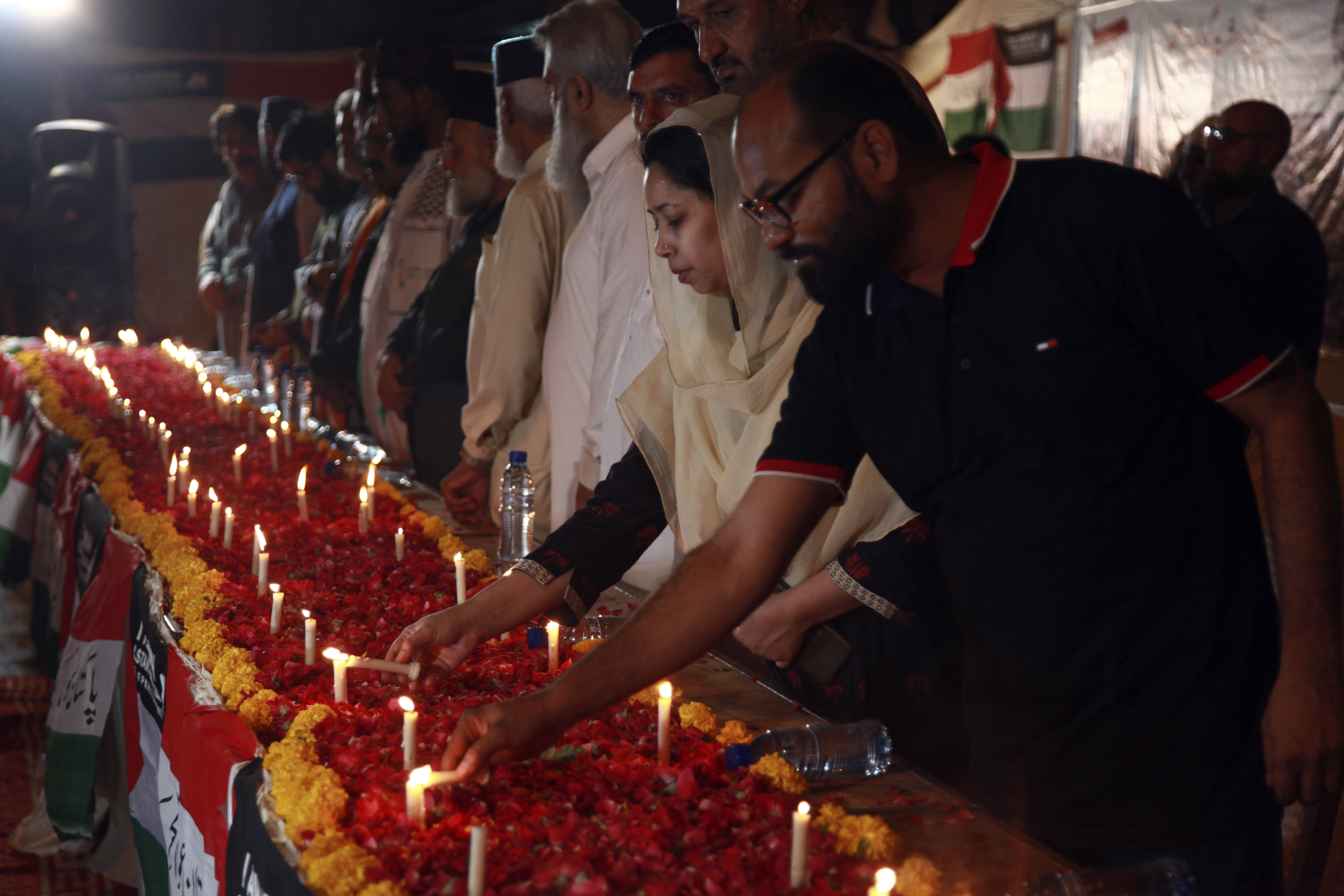 A group of people stand in a row and light candles at a vigil.