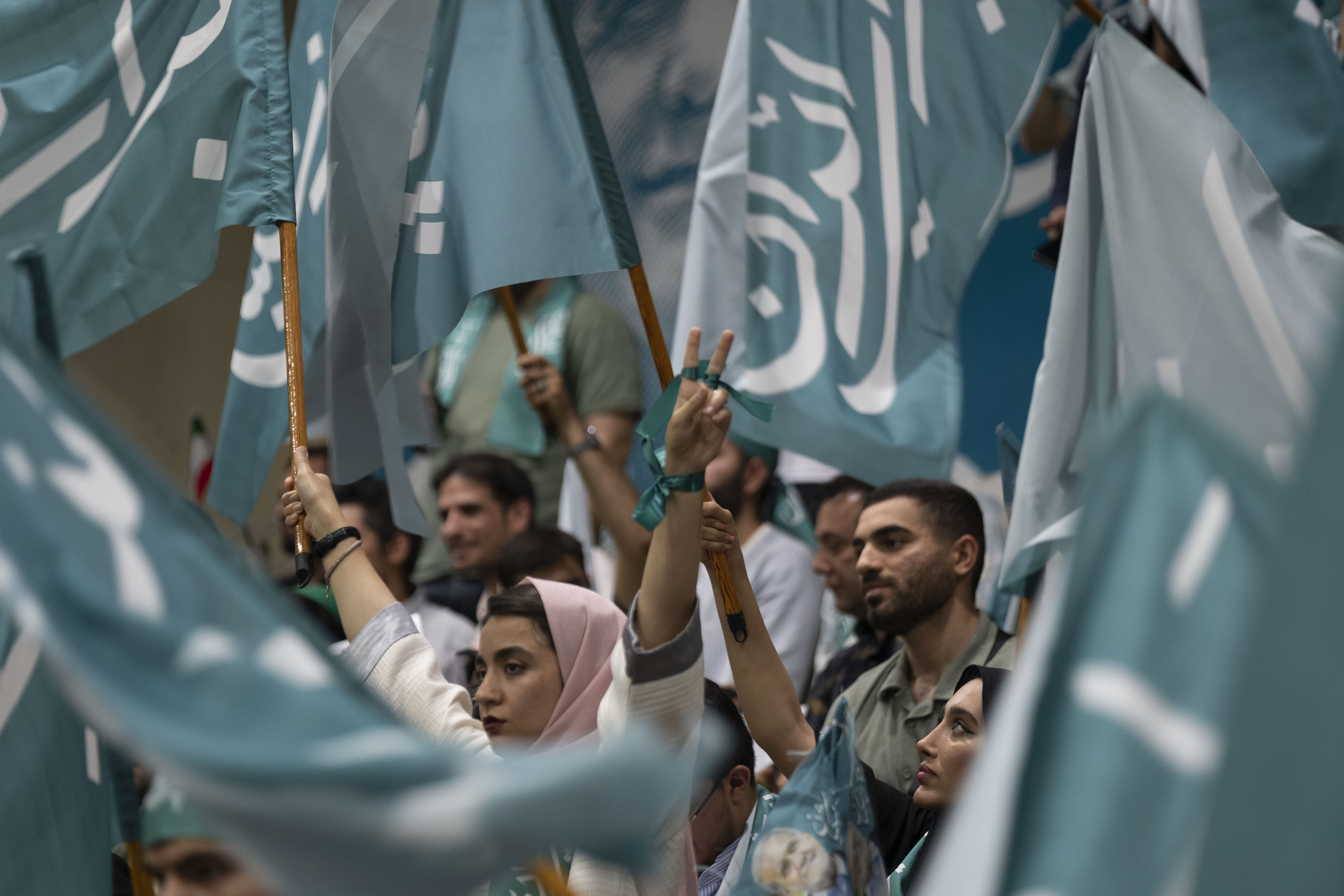 Supporters of Iranian President Pezeshkian wave blue flags and display the ‘Victory’ sign during his election campaign