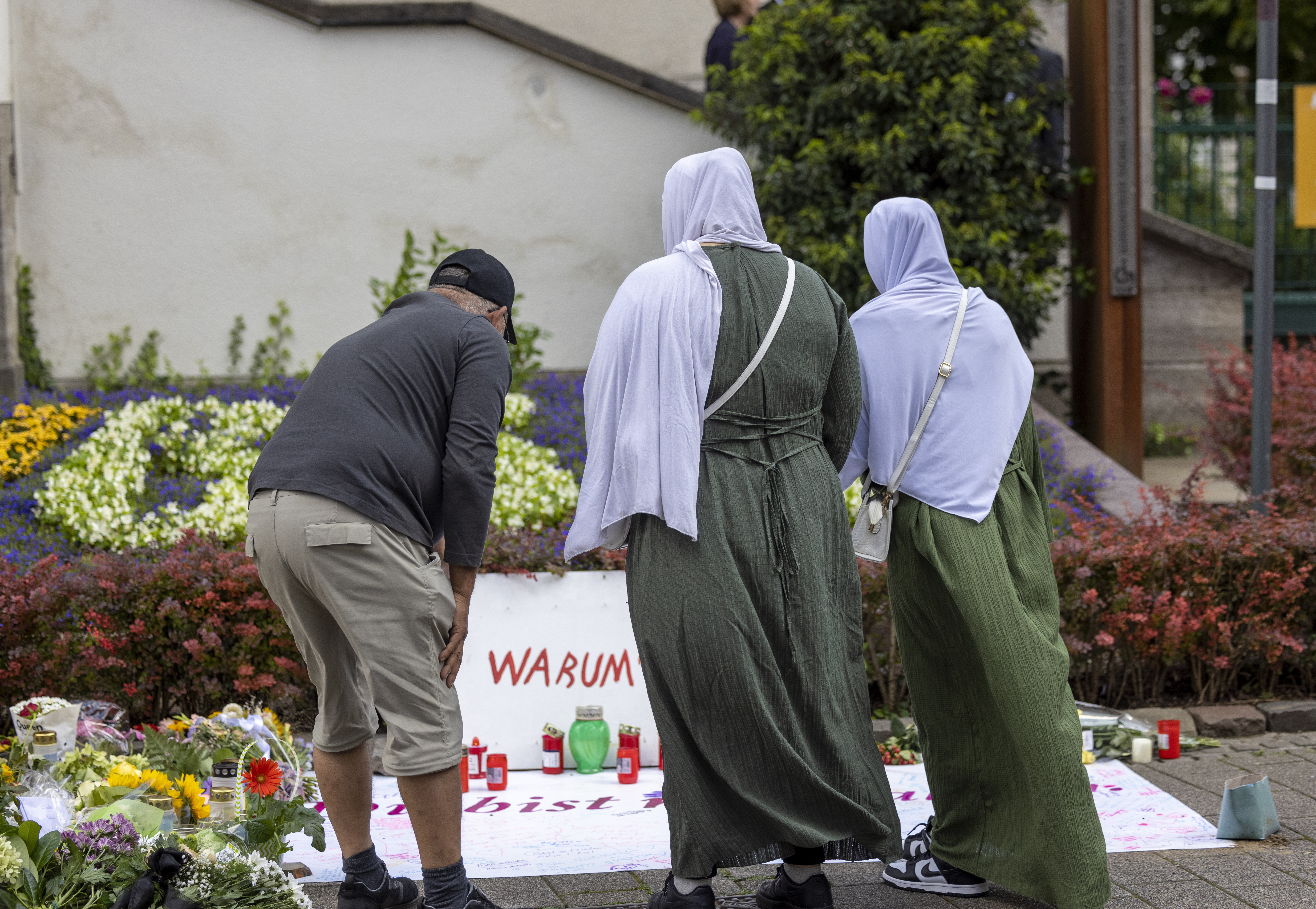 Ein Mann und zwei Frauen mit Kopftuch stehen vor einer Gedenktafel für die Opfer des Messerangriffs in Solingen.