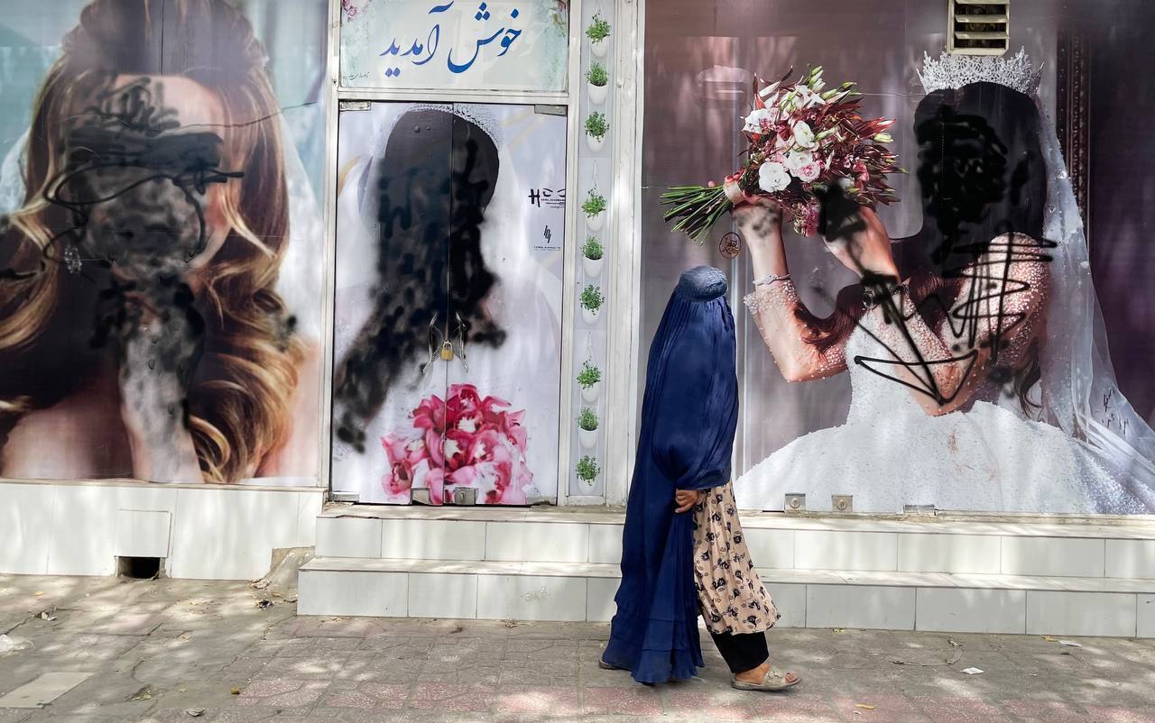 A veiled woman walks past a beauty parlour. The faces of the women on the adverts on the wall are painted over in black.