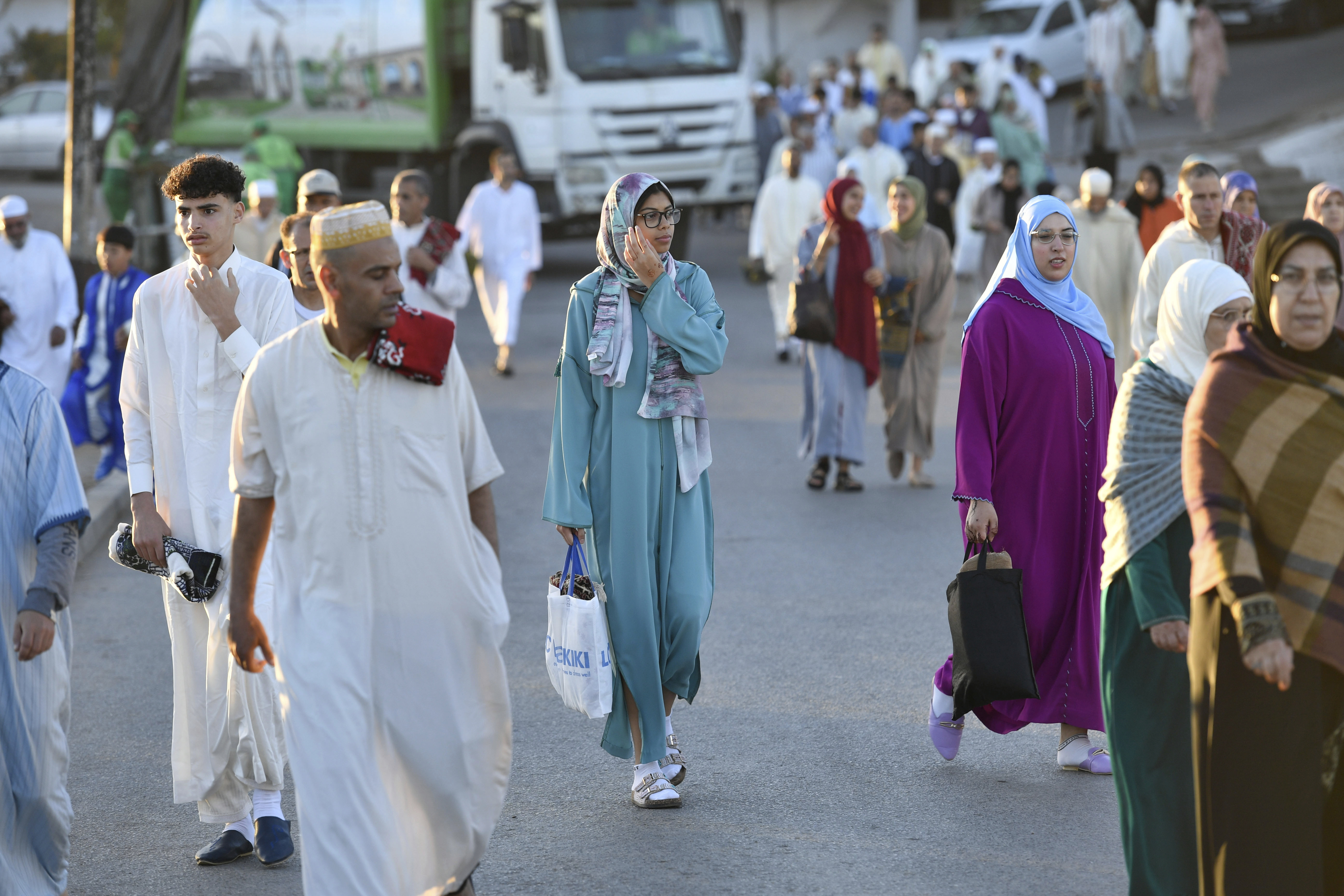 A group of people in robes, women wearing headscarves, walk down a street in early morning light..