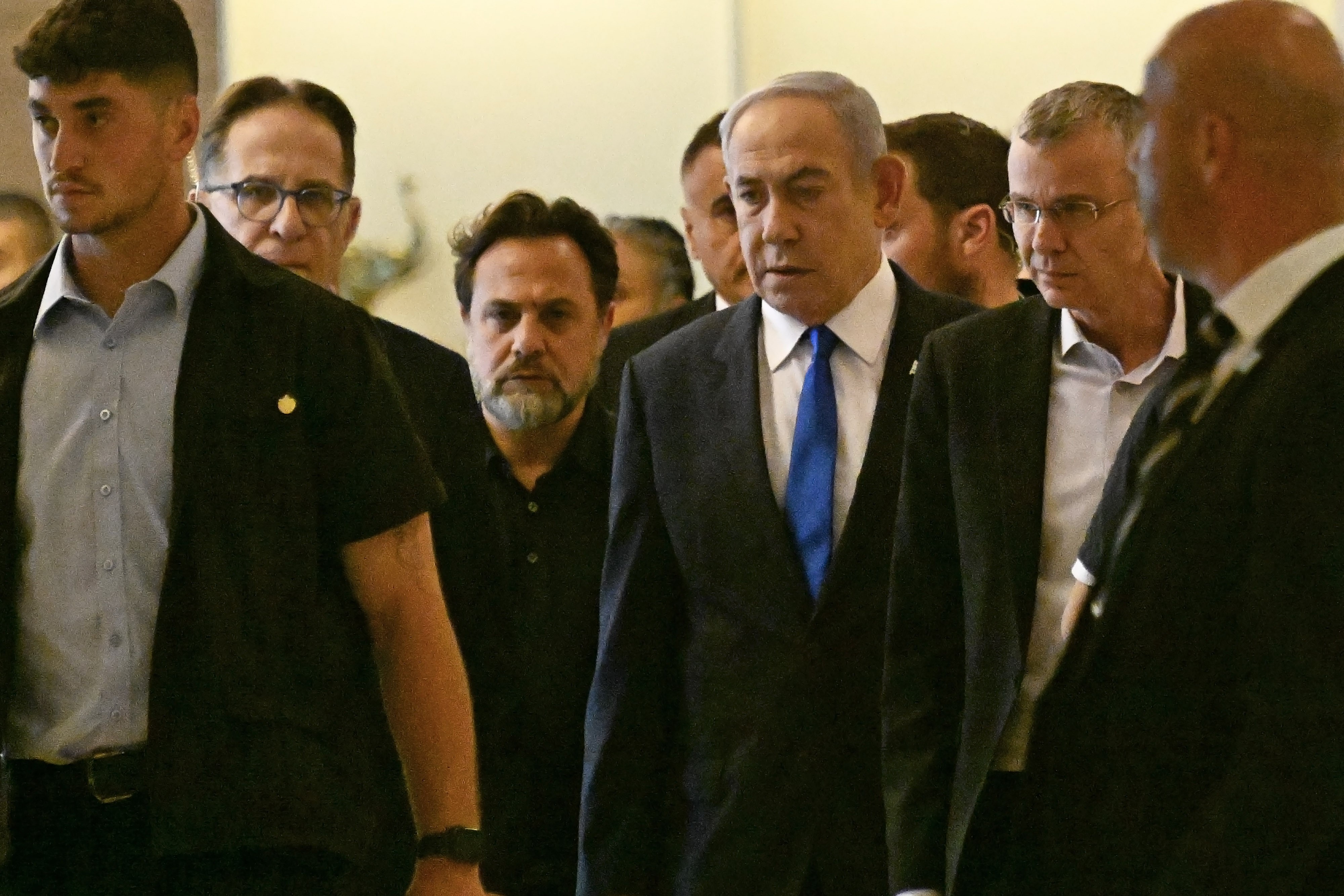 Netanjahu mittig im Bild, läuft umgeben von Männern im Anzug im Gebäude in der Knesset.