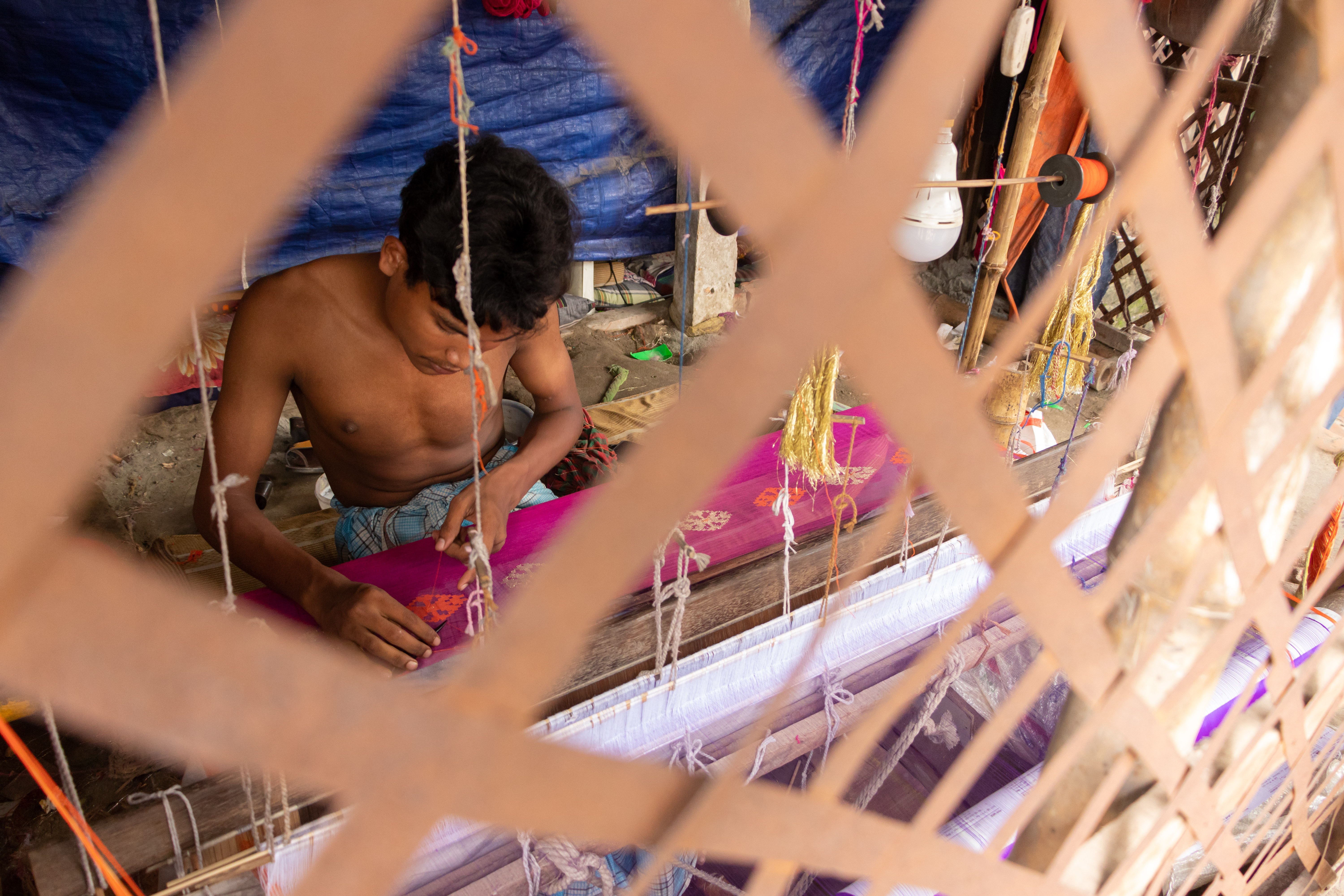 Ein kleiner Junge näht in Bangladesch einen Sari