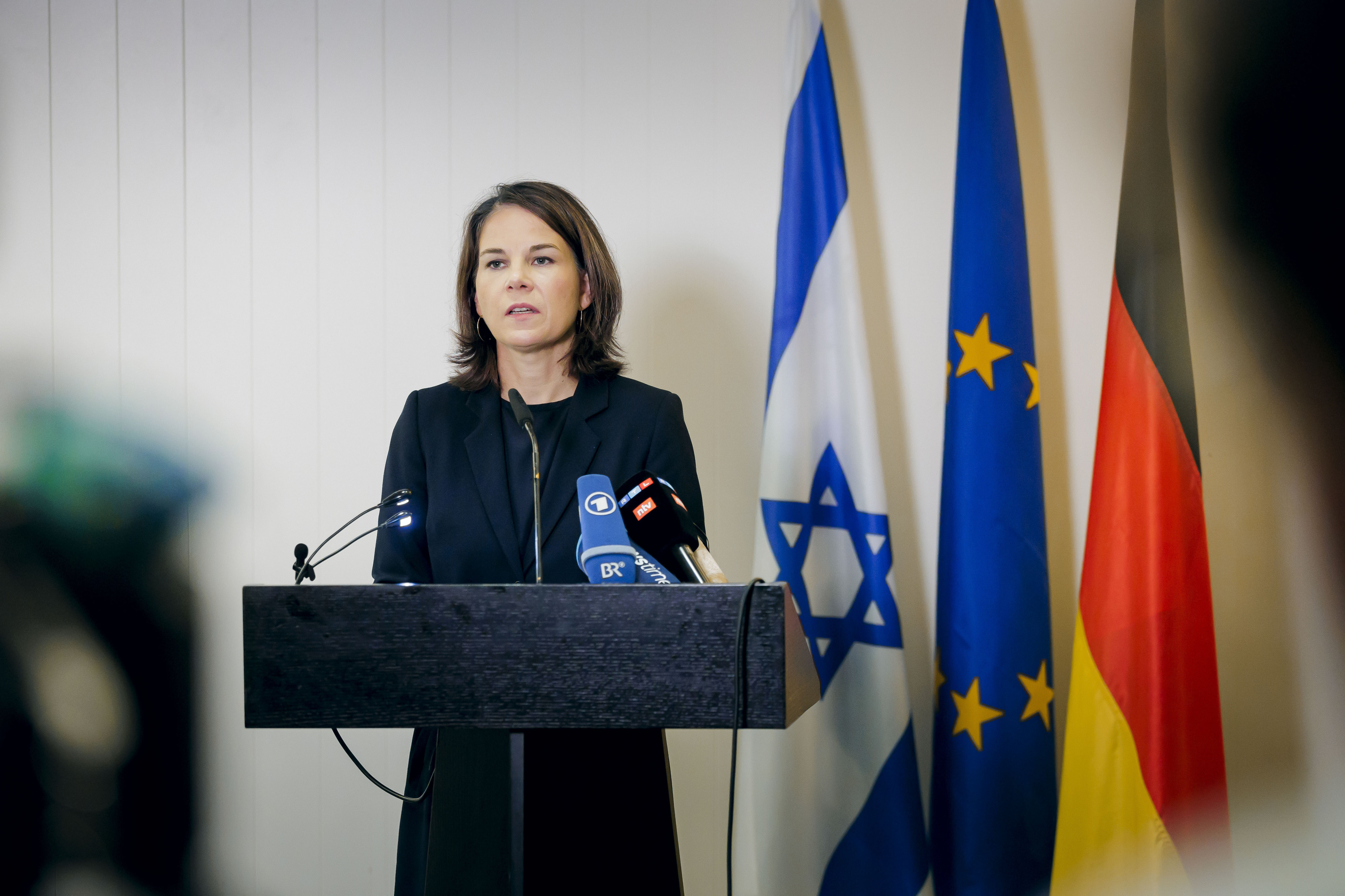 Baerbock makes a statement in front of an Israeli flag, a European flag and a German flag.