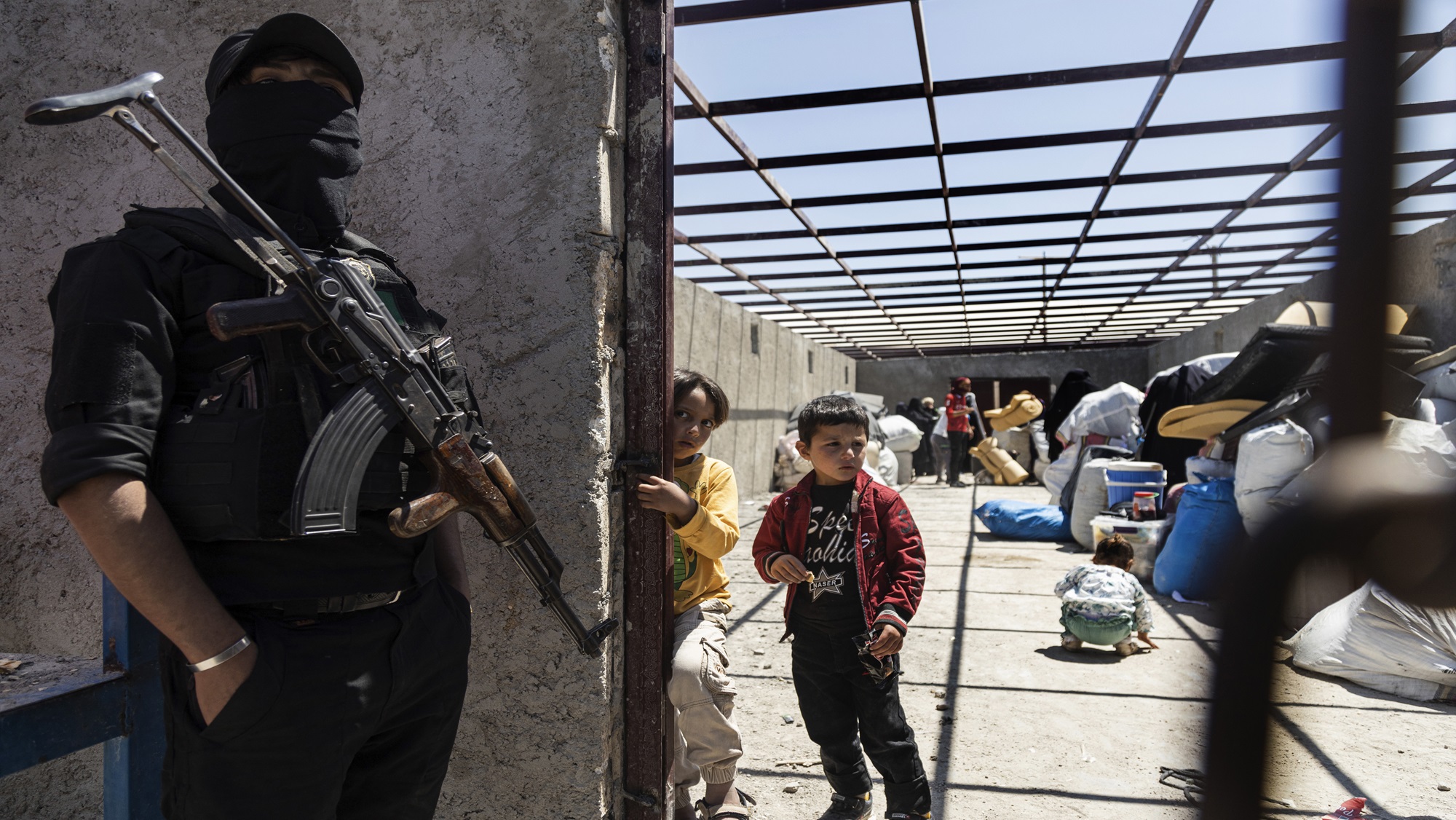 A fighter stands guard where family members of suspected Islamic State group fighters gather and wait to be transferred from al-Hol camp, Syria.