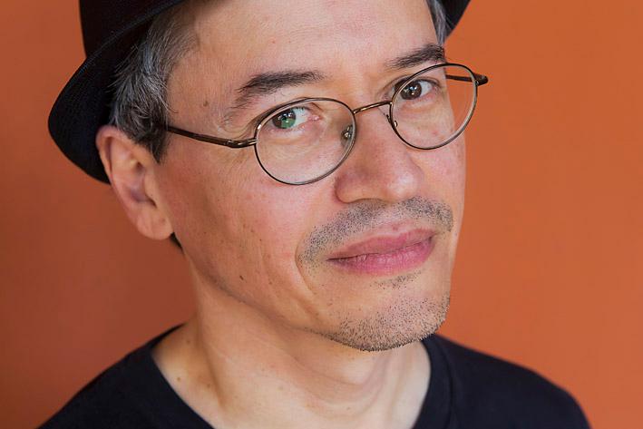 Close-up portrait of Joe Sakho wearing a black T-shirt, glasses and a black hat.