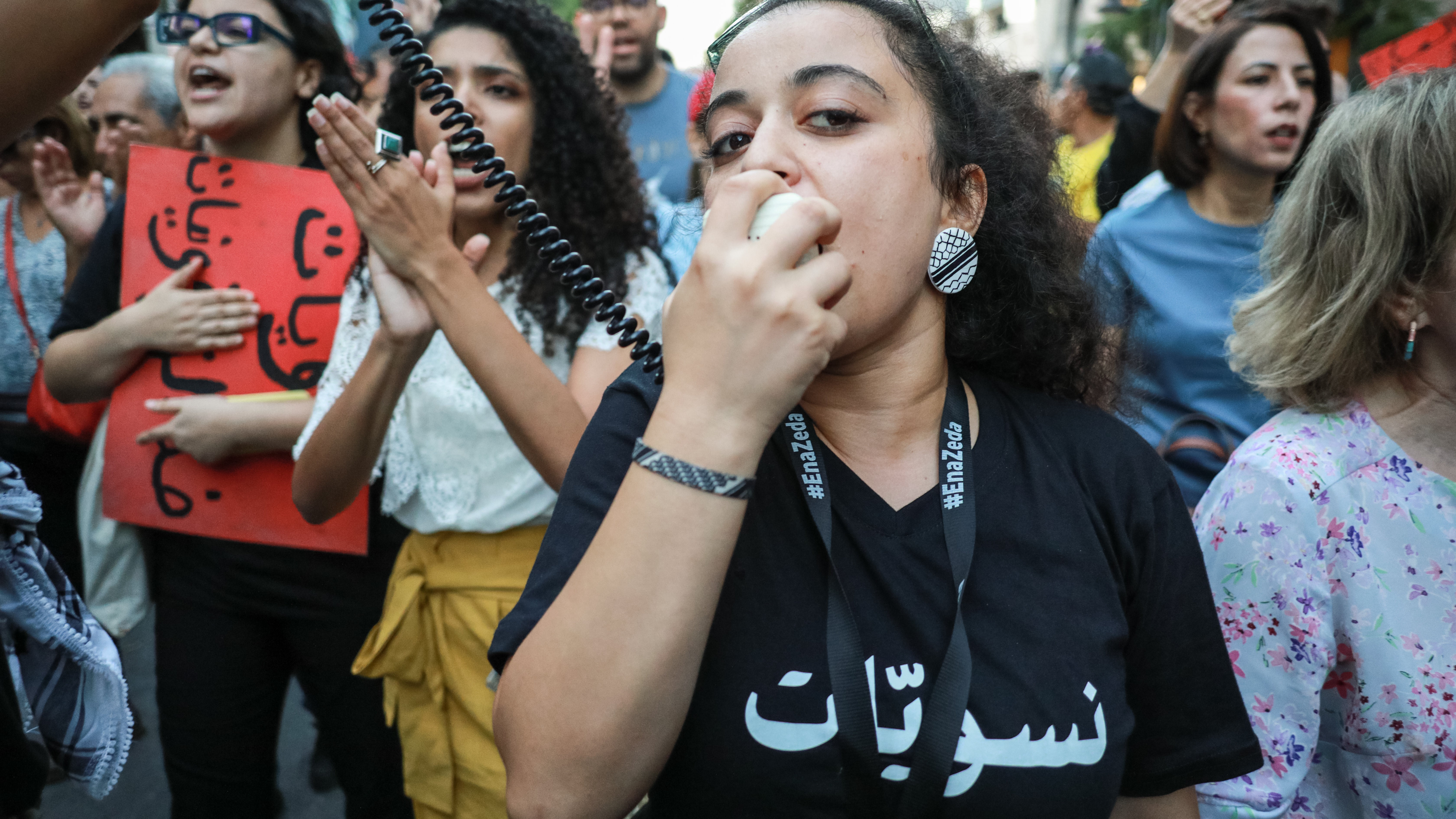 A woman speaks into a megaphone at a demonstration, other women walk behind her.