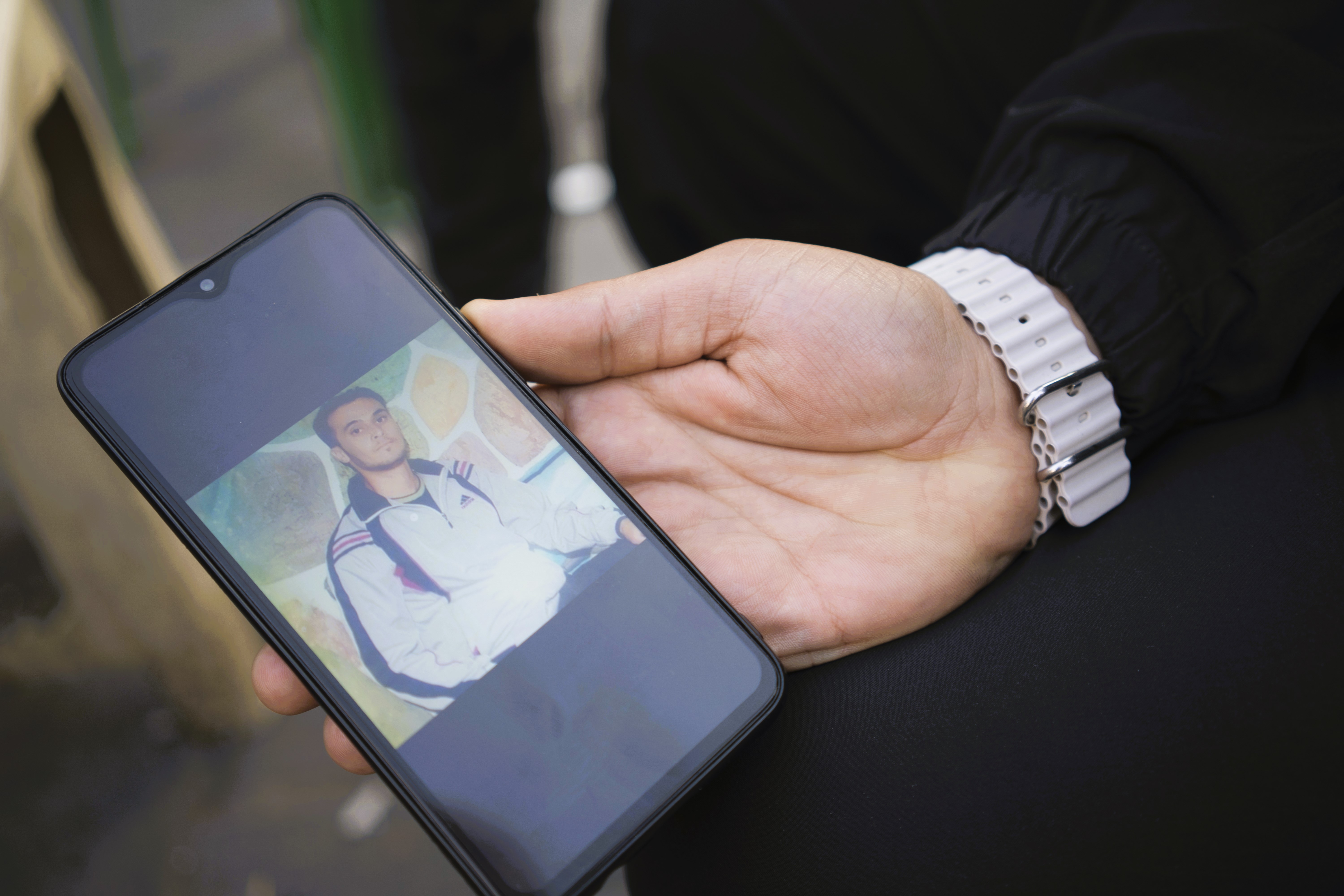 An phone is held up to the camera with a photo of a man in a track jacket on the screen.