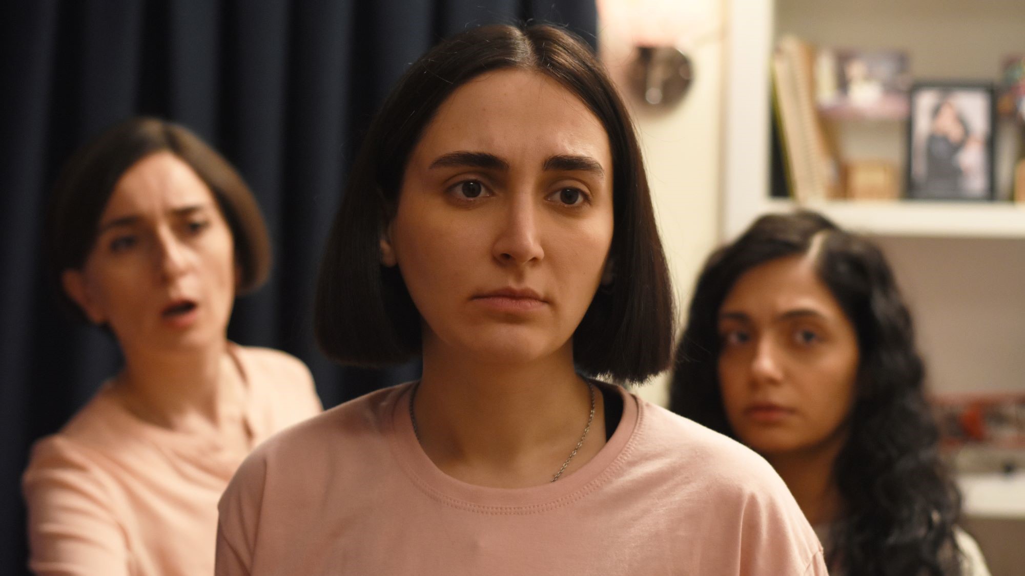 In the foreground close-up of a young woman, behind her on the right and left an older woman and a girl.