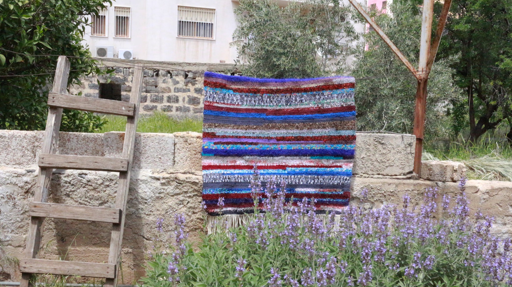 A blanket hangs on a piece of string outdoors, surrounded by plants.