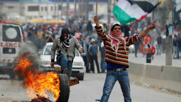 A Palestinian protester rolls a burning tyre down a street during clashes with Israeli security forces at Qalandiya checkpoint near Ramallah (photo: REUTERS/Mohamad Torokman)