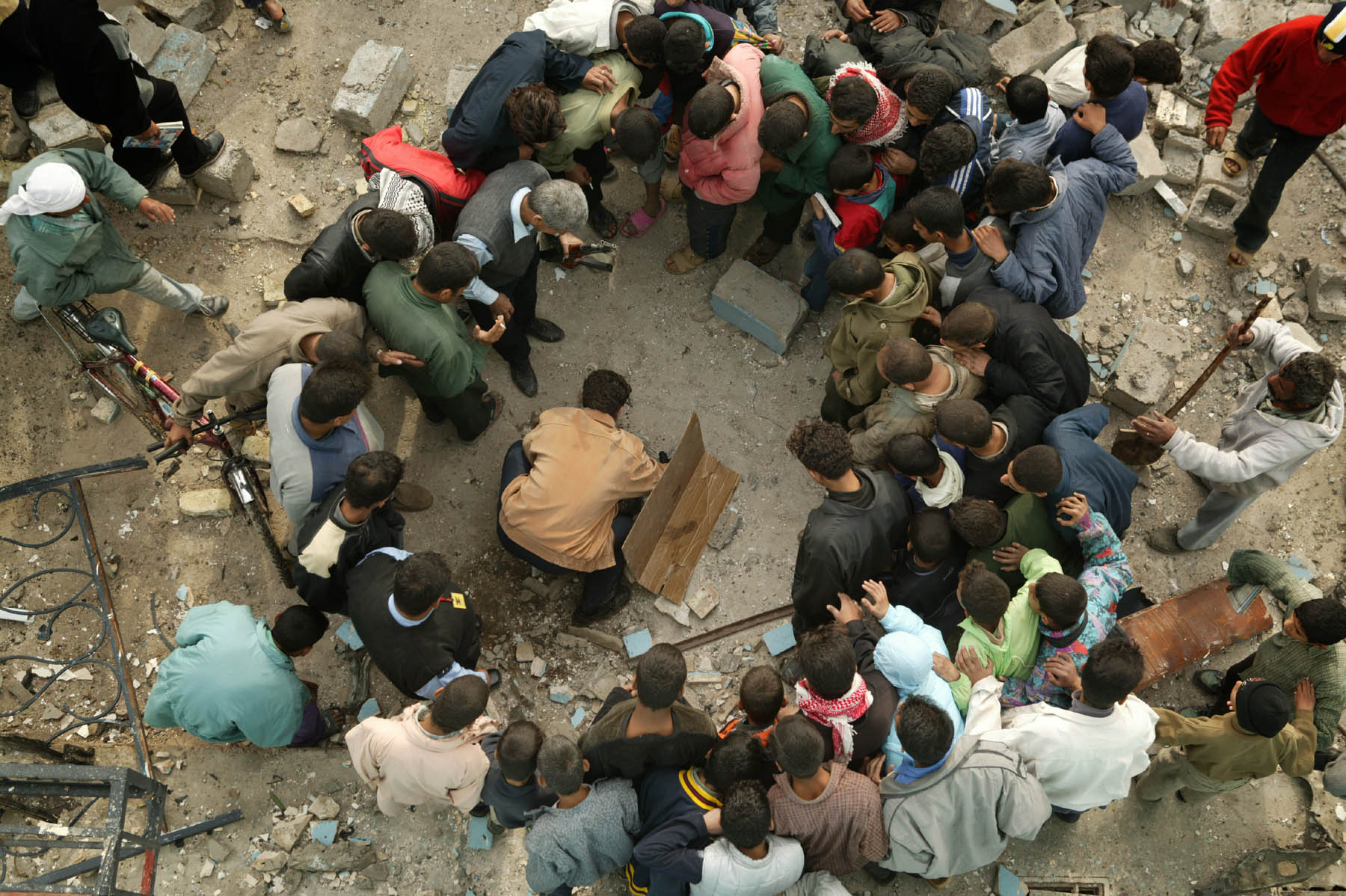 Iraqis gawking at a severed foot and part of a head, remnants of a suicide bomber, which were being removed by a police officer, centre, outside a police station in Husseiniya, Iraq, 15 December 2003 (photo: Michael Kamber) 