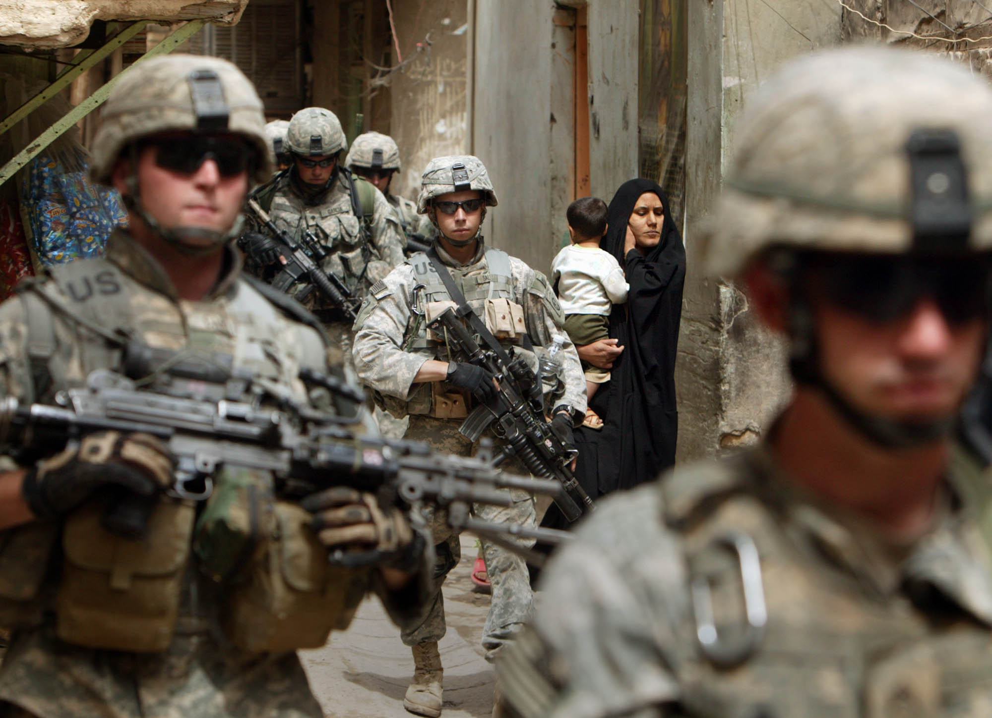 US soldiers patrolling the streets of Khadamiya pass an Iraqi woman carrying her child in her arms (photo: Michael Kamber)