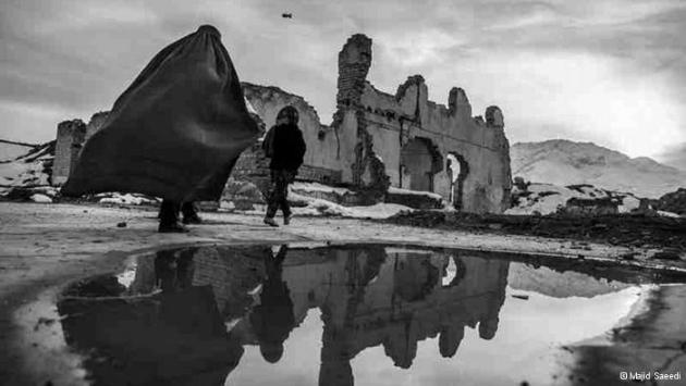 An Afghan woman and child walk past a ruined house (photo: Majid Saeedi)