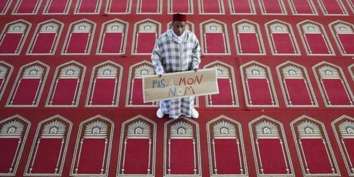 A man holds up a sign that reads #PasEnMonNom (Not in my name) (source: #PasEnMonNom)