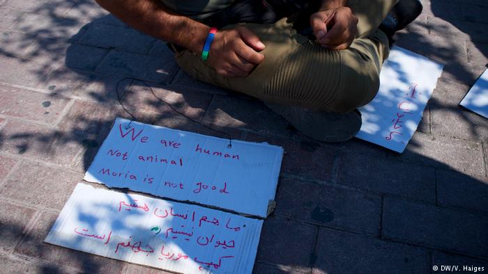 A man sits behind protest signs placed on the ground