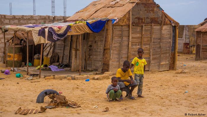 A young boy stands in front of a makeshift house