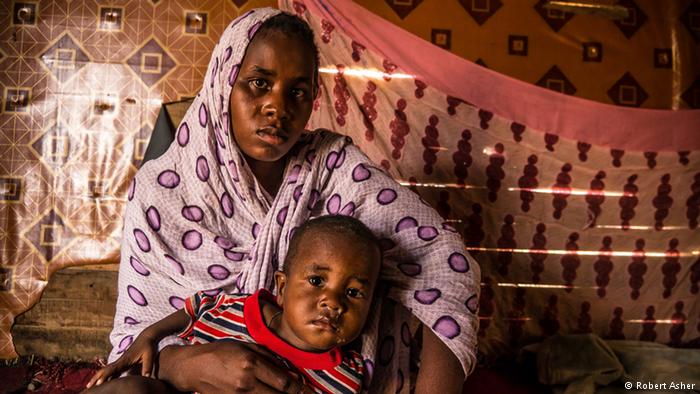 Dressed in a patterned scarf, Mbarka sits holding a young boy