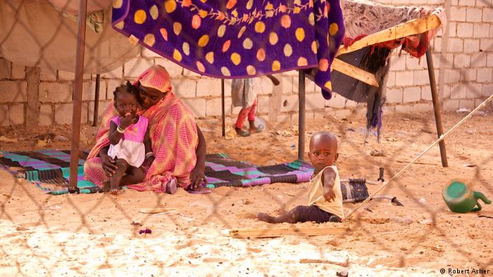 A woman sits on a dirt floor caring for a child