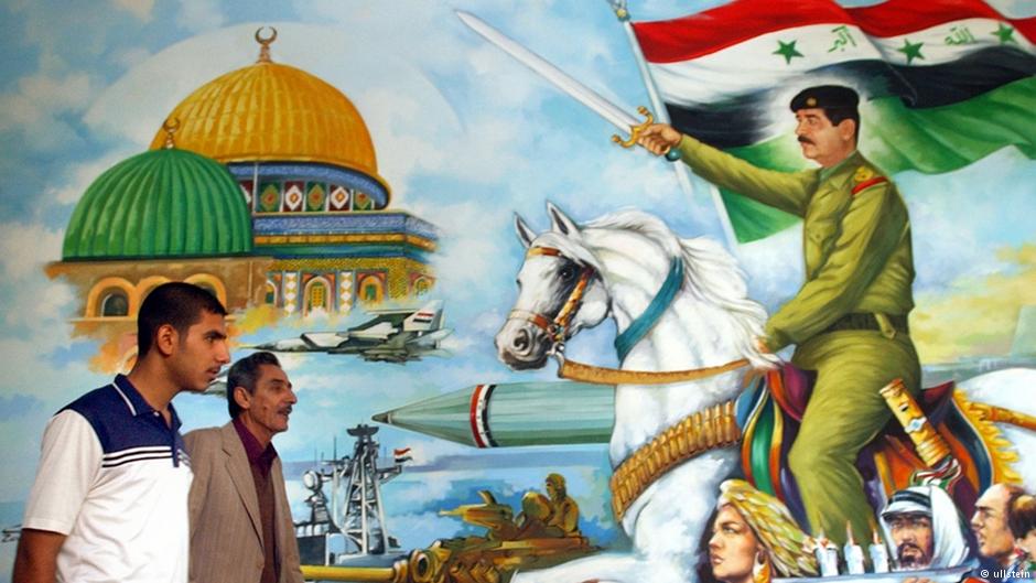 Männer laufen an einem Poster des Saddam Art Center in Bagdad vorbei, das Iraks ehemaligen Staatspräsidenten Saddam Hussein in kriegerischer Pose sowie die Al-Aksa-Moschee in Jerusalem zeigt; Foto: AP 