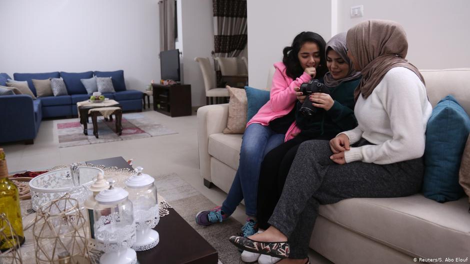 Nada Rudwan (centre), 27, a graduate of English faculty, watches videos of her filmed by her sister Lama Rudwan (right), 22, while cooking, in their home in Gaza City (photo: Reuters/Samar Abo Elouf)