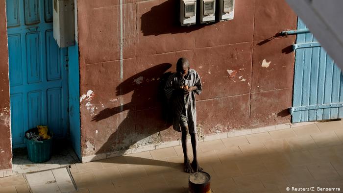 A talibe eats as he begs in front of a hotel (photo: Zohra Bensemra)