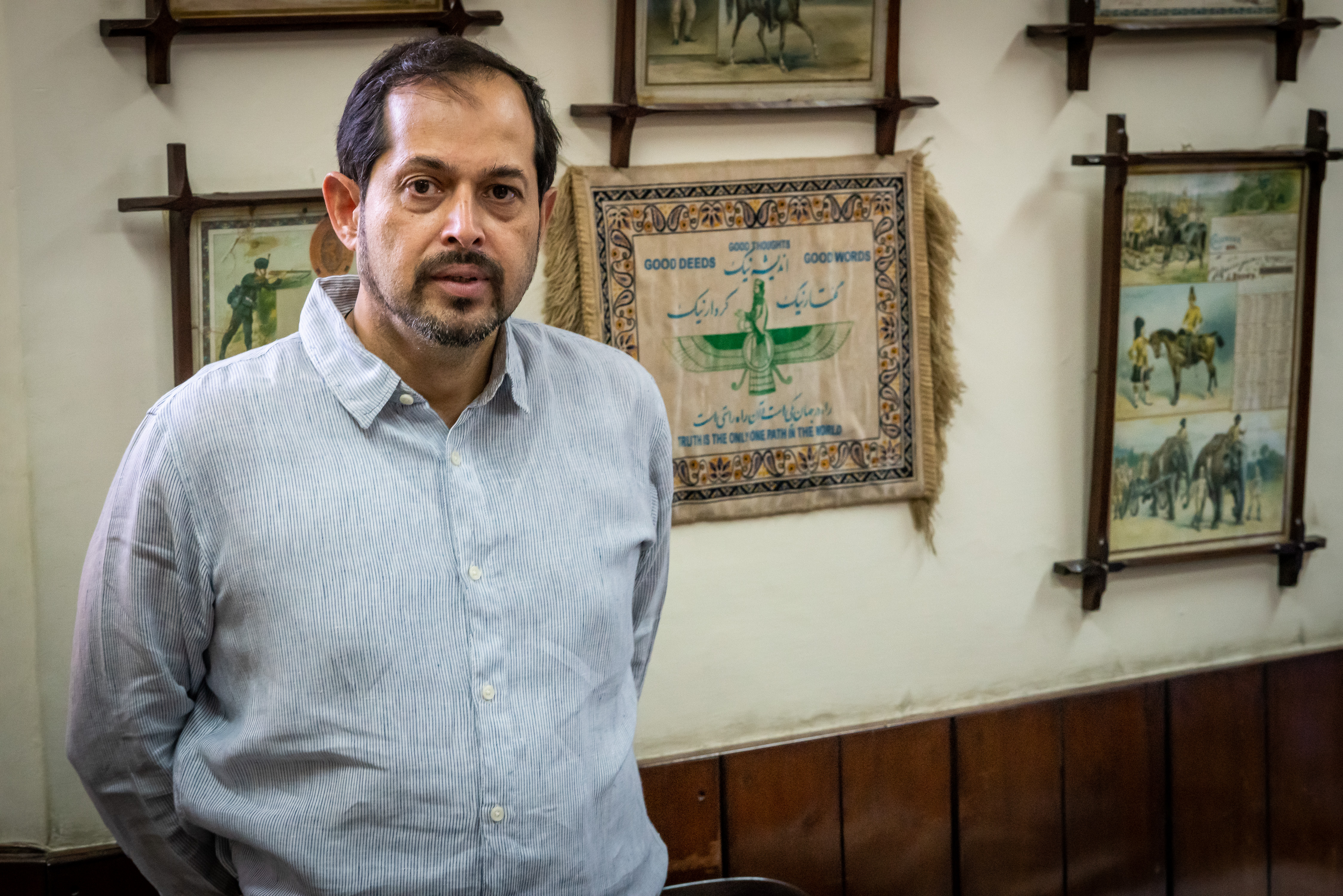 Isphanyar Bahndara steht in seinem Büro für ein Porträtfoto. Im Hintergrund hängt ein Teppich mit den wichtigsten religiösen Credo der Parsen: "Gutes Denken, gutes Handeln, gute Worte"; Foto: Philipp Breu