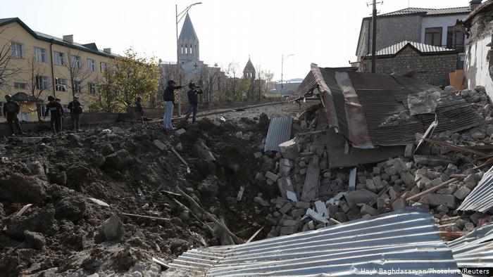 Ruins of destroyed buildings; several people and a church spire in the background, Shusha, Nagorno-Karabakh (photo: Baghdasaryan/Photolure/Reuters) 