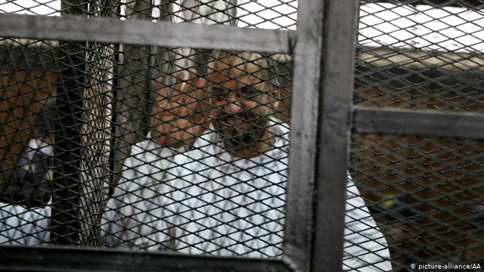 Mohammed el-Beltagy waves from behind bars during his trial in 2014