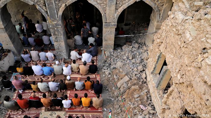 People pray next to the ruins of Al-Masfi mosque in Mosul, Iraq