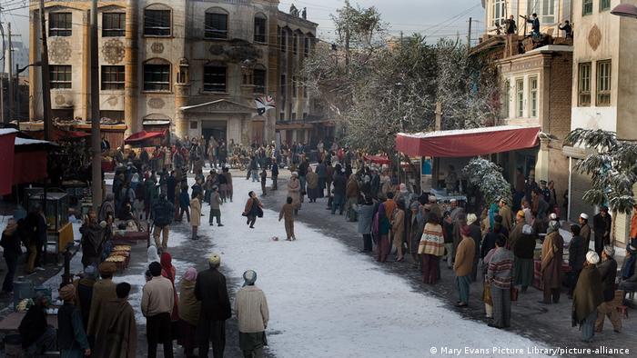 People crowded along a snowy path while children fly a kite