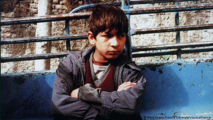 A boy standing against a wall with his arms crossed