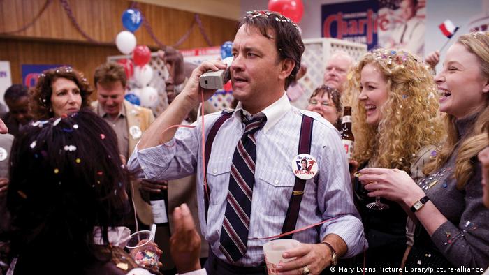 Man speaking on a 1980s cell phone at an election celebration, people smiling in the background