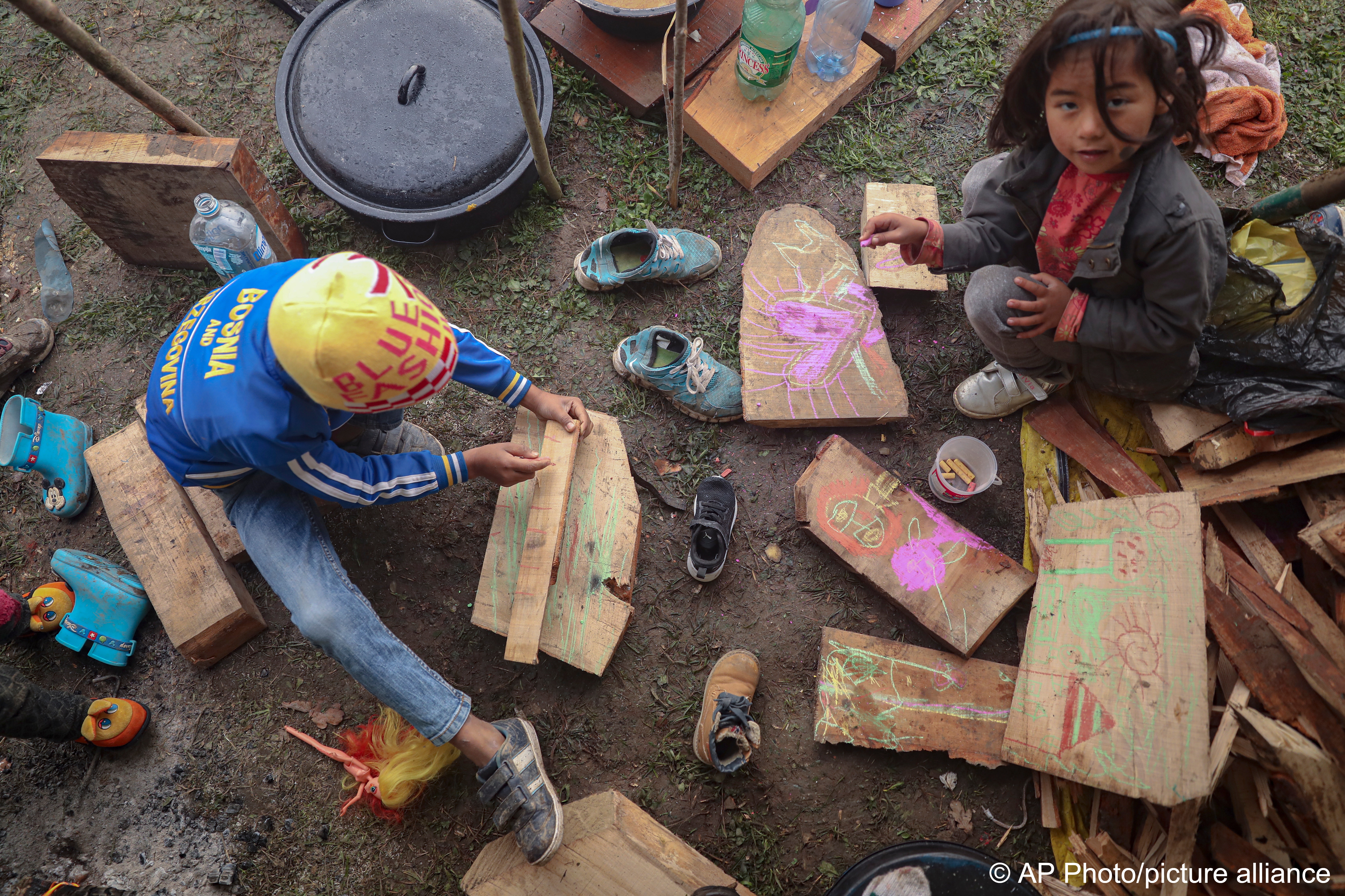 Migrant children draw on pieces of wood at a makeshift camp housing migrants mostly from Afghanistan, in Velika Kladusa, Bosnia, 12 October 2021 (photo: AP Photo)