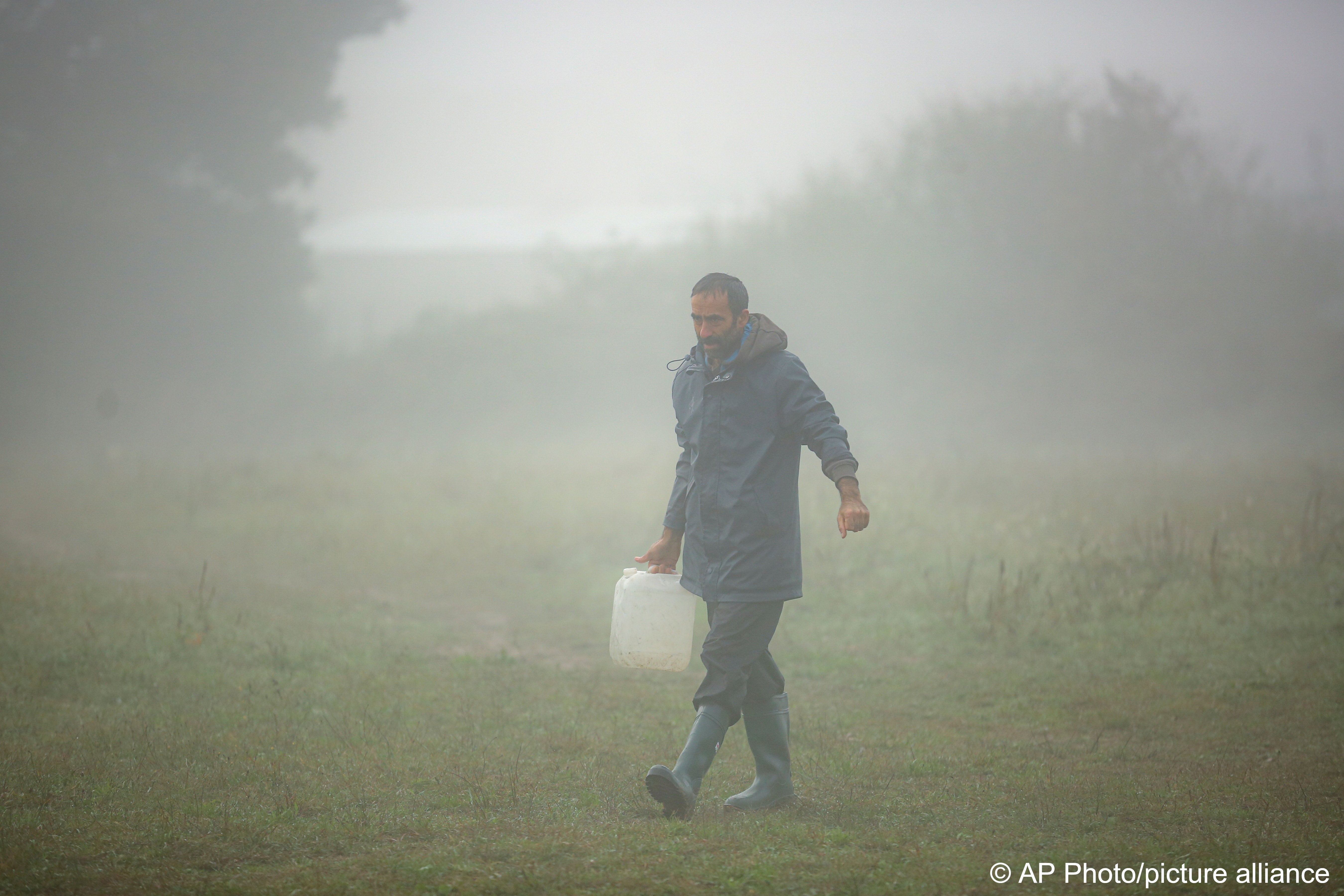 Ein Migrant trägt an einem nebligen Morgen Trinkwasser in einem behelfsmäßigen Lager für Migranten, die hauptsächlich aus Afghanistan stammen, in Velika Kladusa, Bosnien, am 12. Oktober 2021; Foto: AP Photo